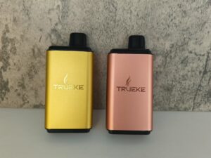 Elegant gold and copper vaping devices showcasing TRUEKE branding against a textured gray background.